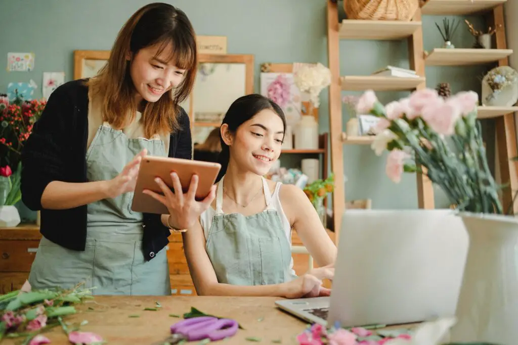 happy-multiracial-women-working-on-gadgets-in-floral-store