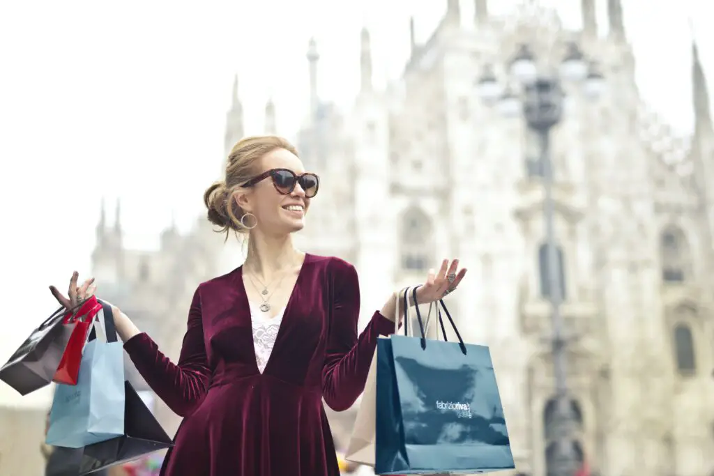 rich vs wealthy woman wearing maroon velvet plunge neck long sleeved dress while carrying several paper bags