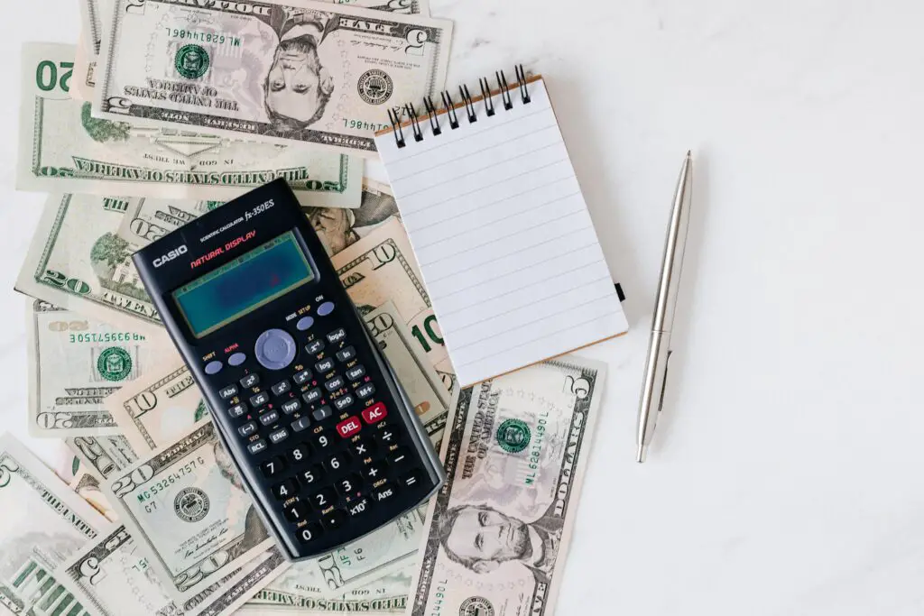 flat lay photo of calculator, pen and paper, dollar bills