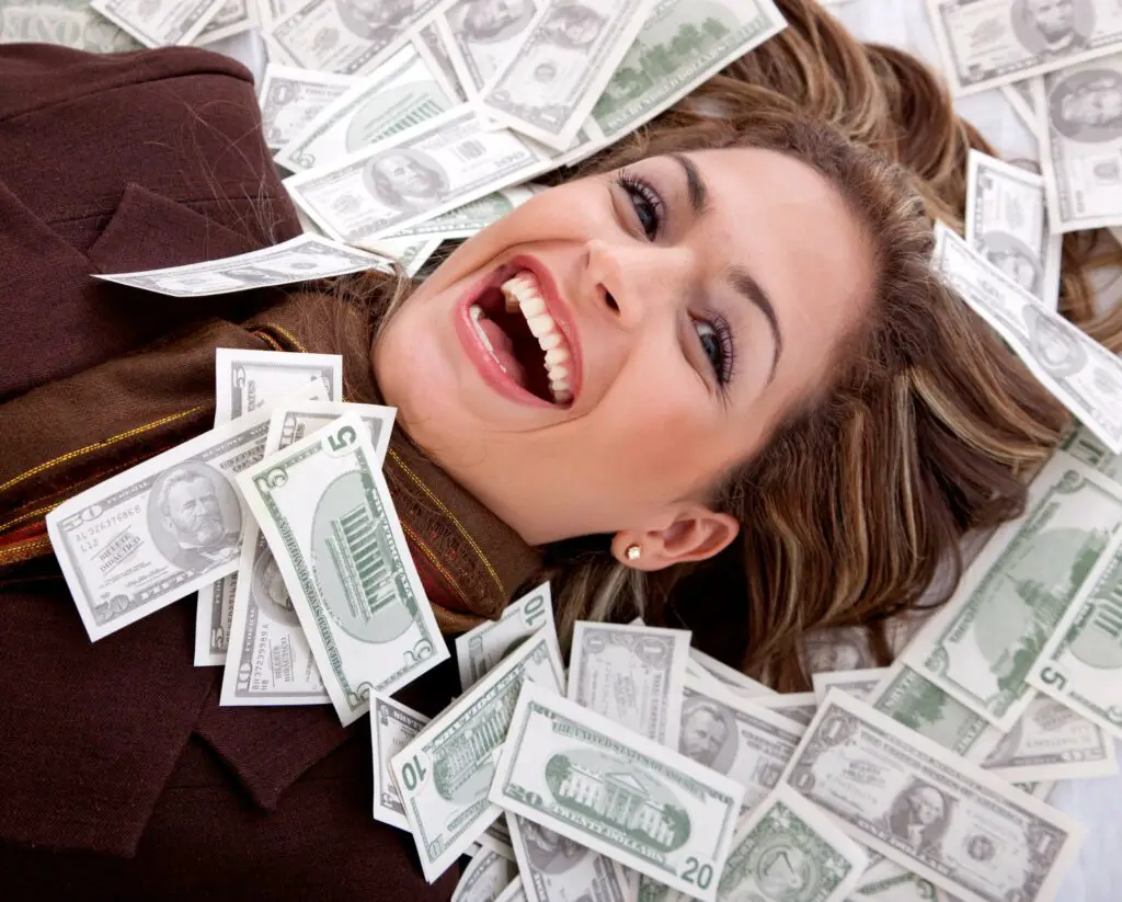 smiling woman lying on stash of money bills 